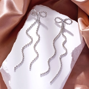 Detail of silver bow earrings with long rhinestone tassels on champagne silk fabric