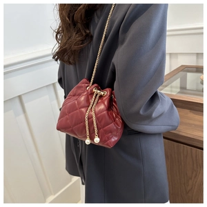 Detail of burgundy quilted bucket bag featuring gold chain strap and pearl accents