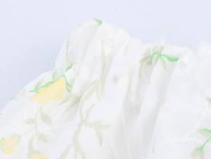 Dettaglio di tessuto floreale con ricamo a occhielli bianchi e design a nido d'ape