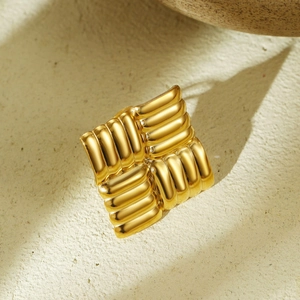 Detailed close-up of a ribbed 18K gold plated titanium steel square earring on stone