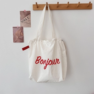 Detail of white canvas tote bag with red Bonjour lettering hanging on a wooden rack