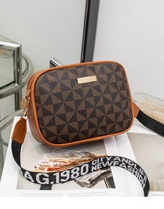 Close-up of a brown geometric crossbody bag with a wide branded canvas strap on a magazine