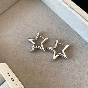 Macro detail of polished silver star-shaped hoop earrings on a grey velvet jewelry box