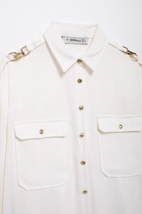Detailed close-up of white crepe blouse featuring gold buttons and shoulder strap accents