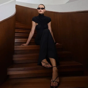 Detail van een elegante zwarte jumpsuit met hoge hals en wijde pijpen op houten trap