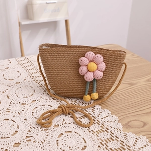 Détail du sac à bandoulière en paille avec fleurs au crochet roses et pompon jaune