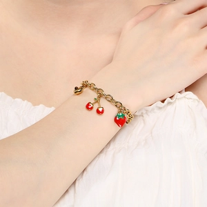 Détail d'un bracelet doré avec des breloques en émail fraise et cerise porté au poignet