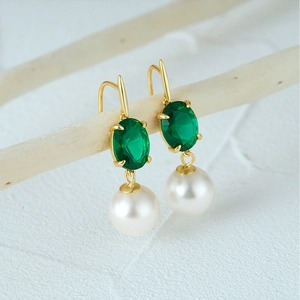 Macro shot of gold emerald green gemstone and white round pearl drop earring