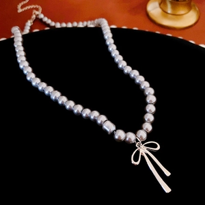Close-up of grey pearl choker necklace with gold bow pendant on black velvet fabric