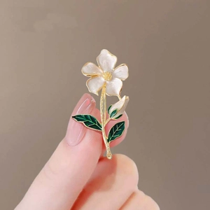 Elegant white floral brooch with gold stems and green leaves held in hand