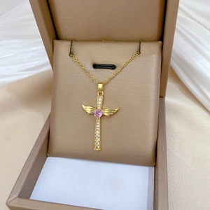 Macro shot of gold cross necklace with angel wings and pink heart-shaped crystal