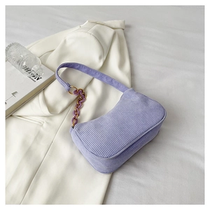 Chic purple corduroy baguette bag with decorative chain on a fashion magazine background