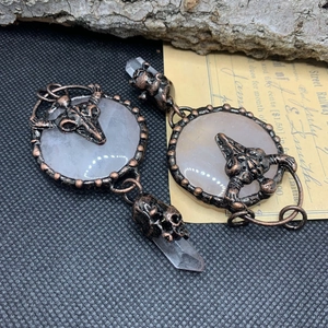 Close-up of vintage bronze skull pendant with white stone and clear crystal column detail