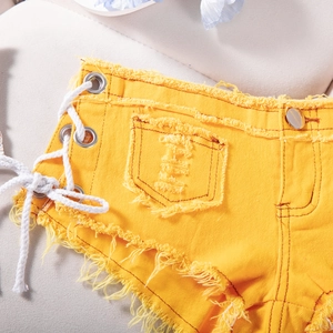 Dettaglio degli shorts in denim giallo con lacci laterali e bordi orlati sfilacciati