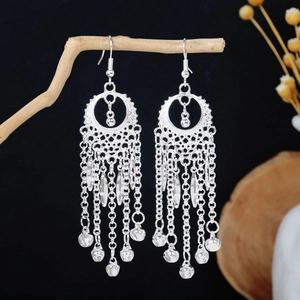 Dettaglio orecchini etnici a nappa color argento con campanelli su supporto in legno