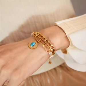 Close-up of double-layer gold chain bracelet with white pearls and turquoise pendant
