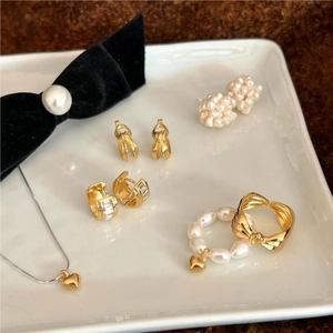 Flat lay of gold knot earrings and pearl heart jewelry set on a white ceramic tray