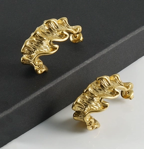 Close-up of golden asymmetric titanium steel earrings with artistic wavy texture