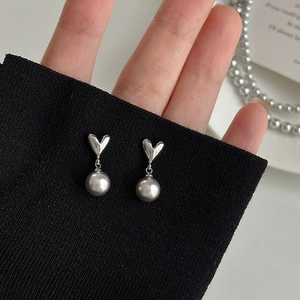 French luxury heart earrings with grey pearls hanging from silver studs on black fabric