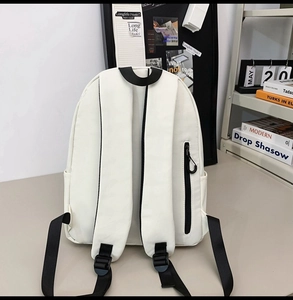 Detail of white canvas backpack featuring black straps and a secure rear zipper pocket