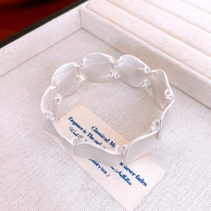 Detailed view of silver wavy geometric bracelet resting on soft beige jewelry cushion