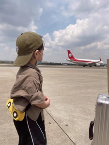 Outdoor shot of a child wearing a dark green cap and a yellow car-shaped crossbody bag