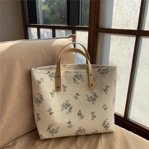 Close-up of floral tote bag with brown leather handles and gold rivets on a sofa