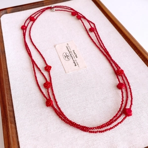 Multi-layer red glass beaded necklace with rose flower charms on a rustic display tray