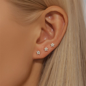 Detailed view of three gold S925 silver triangle flower stud earrings worn on the ear
