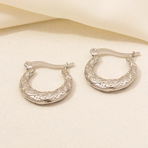 Macro detail of silver vintage-style hoop earrings featuring intricate floral relief patterns