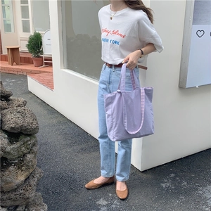 Foto en exterior de un bolso tote de lona lila con correas de cuadros en una modelo