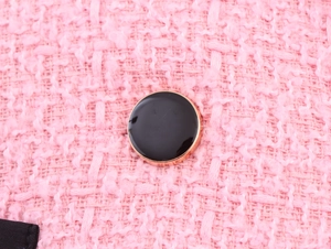 Detailaufnahme von rosa Tweed-Stoff mit einem dekorativen schwarz-goldenen Knopf