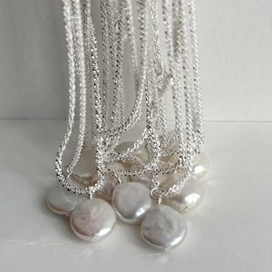 Macro detail of S925 silver shimmering chain with large baroque coin pearl pendants