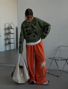 Close-up of oversize green sweater with mushroom print and orange wide-leg trousers