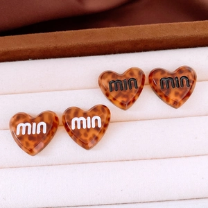 Close-up of tortoise shell heart-shaped earrings with miu lettering on velvet display