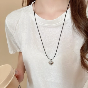 Close-up of a silver heart pendant on a black cord necklace worn over a white T-shirt