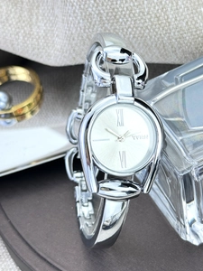 Close-up of silver horsebit watch with roman numerals on a white dial and metal chain band