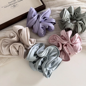 Detail view of five assorted satin scrunchies in pastel colors on textured fabric