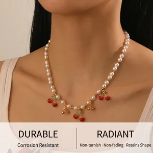 Détail de pendentifs cerises rouges sur un collier ras de cou en perles porté par un mannequin