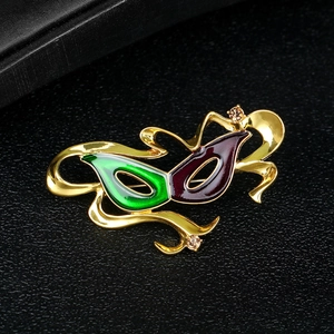 Artistic gold mask brooch with green and purple enamel and rhinestones on black background
