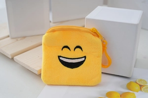 Macro detail of yellow plush coin purse with embroidered smile and plastic carabiner