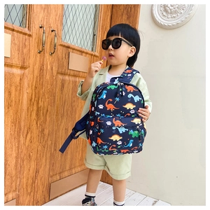 Toddler modeling a navy blue backpack with colorful cartoon dinosaur prints outdoors