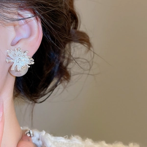 Detailed close-up of a silver flower earring with diamonds and a white pearl on the ear