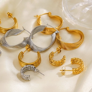 Modern C-shaped gold and silver earrings with layered texture on beige silk background