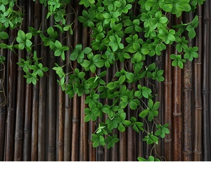 Lush green artificial foliage vine hanging over a natural dark brown bamboo fence