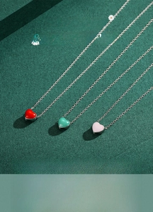 Detailed view of three heart-shaped enamel pendants in red, green, and pink on silver chains