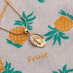 Detailed close-up of golden oval pendant necklace with embossed portrait and crystal border