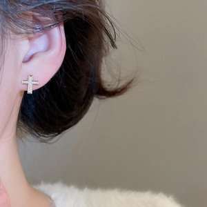 Close-up of golden cross stud earrings with sparkling zircon crystals on model ear