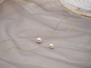 Detailed view of single white pearl on a delicate gold chain over soft grey tulle fabric