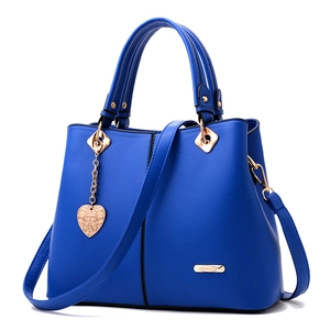 Detail of dark blue leather handbag with gold heart pendant and metallic accents
